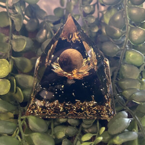 Cette orgonite pyramidale a été fabriqué avec, en son centre, une sphère œil-de-tigre formant la fleur de lotus. Cette même sphère est une protection